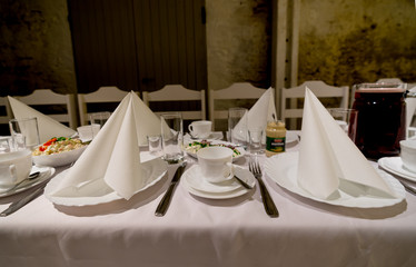 Banquet table, white napkins, elegant simple tableware. Coffee cup in the middle, salad bowl behind...