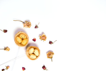 Decorative Easter eggs in nest on white background with dried rose flowers.