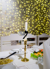Single white candle with black ribbon around. Funeral table to honor dead person. Blurred background from Christmas decoration.