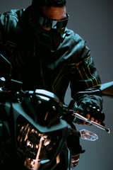 selective focus of mixed race cyberpunk player in mask and futuristic glasses riding motorcycle on grey