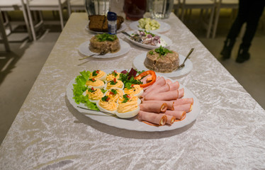 Banquet table waiting for people. Plate with filled eggs and ham rolls. Meat jelly in the background. Traditional food.