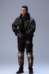 handsome bi-racial cyberpunk player holding gun and standing on grey