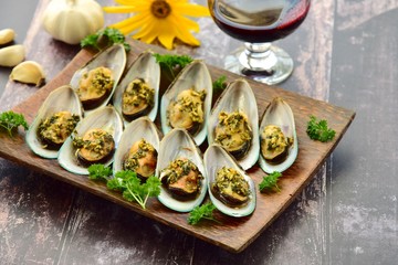 Baked green mussels with garlic butter herb sauce served with glass of red wine
