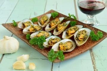 Baked green mussels with garlic butter herb sauce served with glass of red wine
