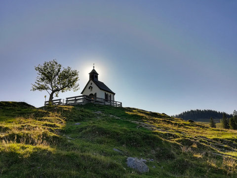 die postalm kapelle auf der postalm zwischen strobl am wolfgangsee salzkammergut und abtenau salzburg im sonnenlicht small chapel at the postalm backlit from sun with halo