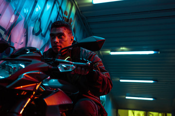 Fototapeta na wymiar low angle view of handsome and mixed race cyberpunk player riding motorcycle