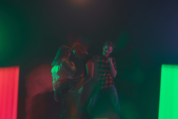 Fototapeta premium Cheering dance party, performance concept. Crowd shadow of people dancing with neon colorful lights raised hands up on dark background. Celebration, holiday, weekend, nightlife and positive vibes.