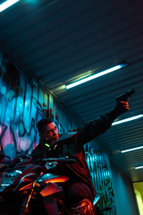 low angle view of mixed race cyberpunk player on motorcycle aiming gun
