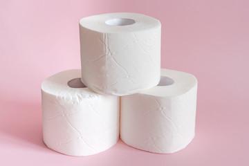 Three rolls of white toilet paper stand on a pink background