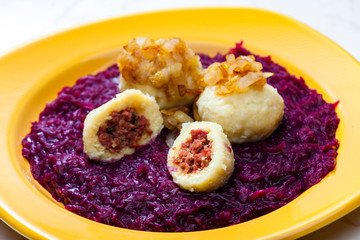 potato dumplings filled with smoked meat with fried onion on red cabbage
