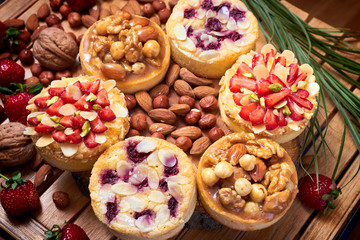 Mini tarts cupcakes with strawberries, walnuts, almond, nuts and blueberries on wooden background. Top view. Close up