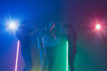 Fototapeta premium Cheering dance party, performance concept. Crowd shadow of people dancing with neon colorful lights raised hands up on dark background. Celebration, holiday, weekend, nightlife and positive vibes.
