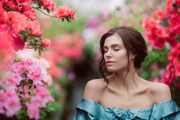 Naklejka premium Beautiful romantic young woman in a greenhouse with azaleas. Art portrait of a girl wearing blue magnificent vintage dress.