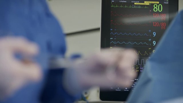 Close up on surgeon hand while stiching. change focus to heart monitor