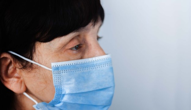 Coronavirus quarantine and Air pollution pm2.5 concept. Face of old sick woman wearing blue respirator mask for protect. Wuhan, China epidemic virus symptoms background.