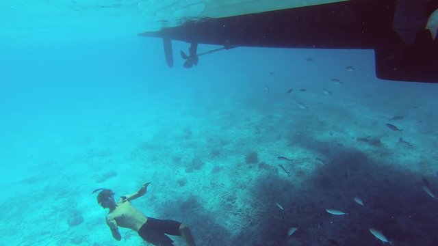 Young man swimming towards the surface of a blue ocean with fish around him