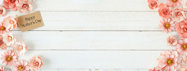 Happy Mothers Day double side border with pink paper flowers and gift tag. Overhead view against a white wood banner background. Copy space.