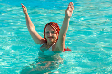 A young woman with African pigtails stands in the water in the pool.