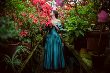 Obraz na płótnie Canvas Beautiful romantic young woman in a greenhouse with azaleas. Art portrait of a girl wearing blue magnificent vintage dress.