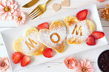 Heart shaped pancakes with MOM letters. Mothers Day breakfast concept. Top view table scene with a...