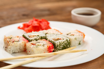 A set of rolls with dill and salmon on a plate with soy sauce, ginger and chopsticks.
