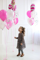 vertical portrait of a cheerful four year old girl in a white studio on a background of balloons