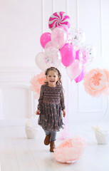 vertical portrait of a cheerful curly four year old girl on the background of balloons and flowers