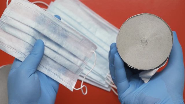 Nurse showing antiviral face masks and rolls lavatory paper on red background. Human hands protected blue medical gloves. Toilet paper, protection masks - concept fight against coronavirus, hygienics.