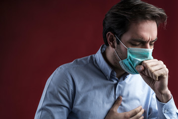 Single sick male standing on background with medical mask and coughing in his hand, studio shoot