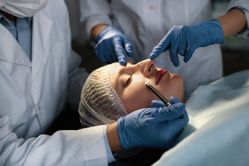 Doctor and nurse preparing female patient for cosmetic surgery in clinic