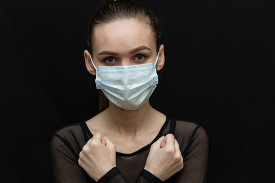 Beautiful girl in a protective mask and with a syringe in her hand. Protect yourself from the virus. Black clothes and background. Protection.