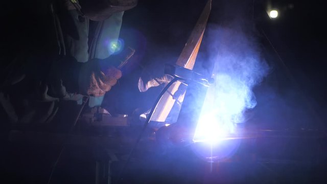 Industrial worker in a protective mask using modern welding machine for welding metal structures in industrial production at a metal processing plant. bright light and sparks from welding.