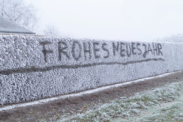 the german word Frohes neues Jahr - Happy new Year written on Snow covered hedges in winter after...