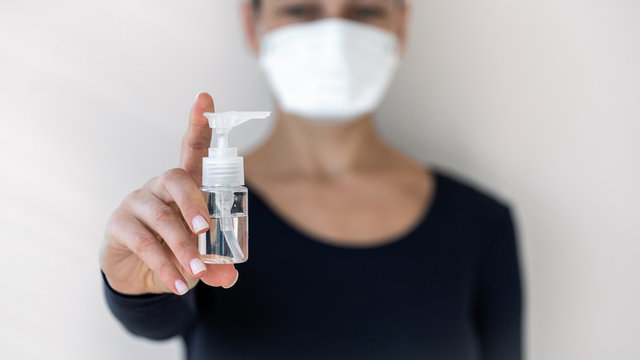 Young Adult Woman In Breath Mask Showing Bottle With Anti Bacterial Gel