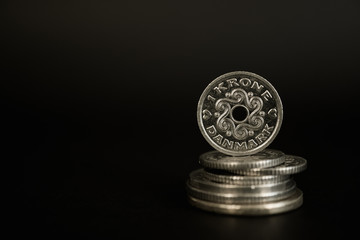 One Danish krone or crown standing on a stack of coins against black background.  High resolution...