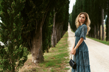 Holiday in Tuscany. Fashion portrait of young happy woman in long dress walking on pathway in typical cypresses alley in Italian countryside