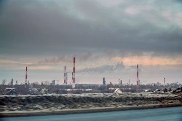 View from the window of a passing car on the Smoking factory chimneys against the overcast sky