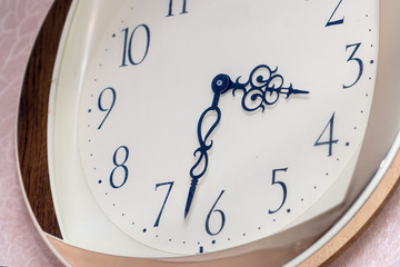 A modern wall clock with a white dial hangs on wall