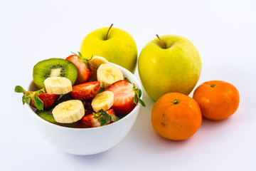 Aerial view of A fruit salad cut in a white bowl on a white background next to tangerines and apples