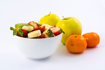 A fruit salad cut into a white bowl on a white background next to tangerines and apples
