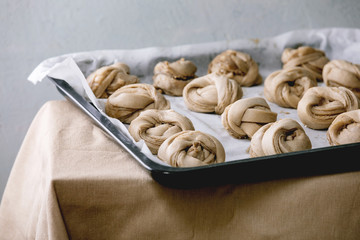 Ready to bake traditional Swedish cardamom sweet buns Kanelbulle on oven tray cover by baking paper on grey linen table cloth.