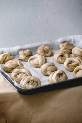 Ready to bake traditional Swedish cardamom sweet buns Kanelbulle on oven tray cover by baking paper on grey linen table cloth.