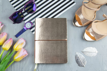 A gold notebook with women's shoes, tulips, glasses and a watch on a concrete background. Flet lay © Вася Фаевич