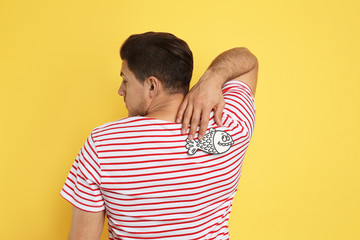 Man with paper fish on back against yellow background. April fool's day