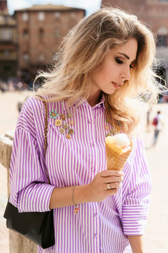 Fototapeta Young female traveler eating traditional italian ice cream called Gelato in the waffle cone in Siena square