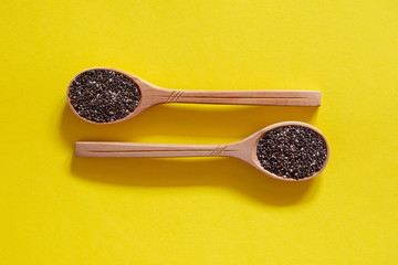 Chia seeds in wooden spoons. Superfood on a yellow background