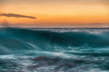 Obraz premium Large wave cresting and breaking at sunset