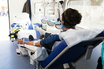 A young donor sitting on an armchair in a mobile blood bank during blood collection. Blood donation...