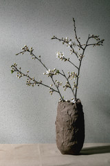 Blossom cherry branches in craft clay vase on grey table cloth. Spring interior decorations.