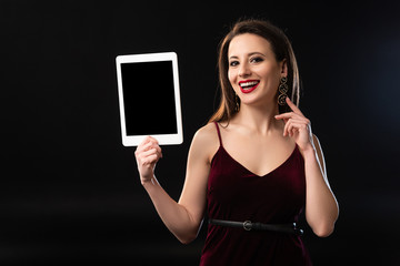 Naklejka premium smiling woman in dress holding digital tablet on black background